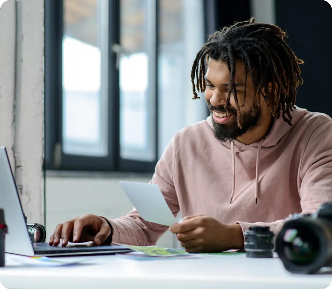 Man smiling while looking at laptop and holding a card