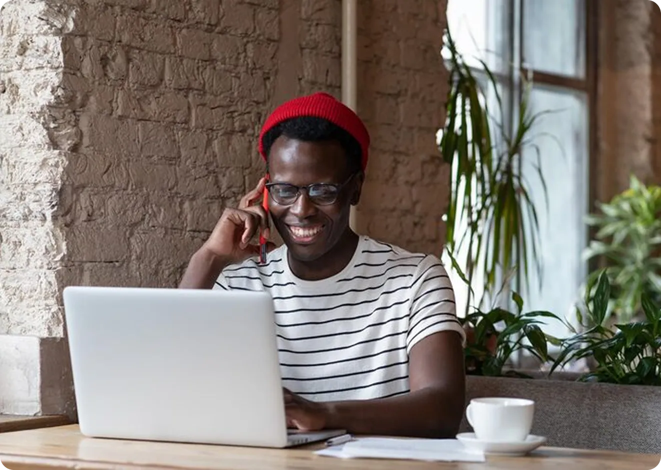 Man smiling in a red beanie using a laptop